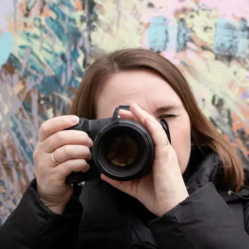 Woman looking through camera in front of painted wall