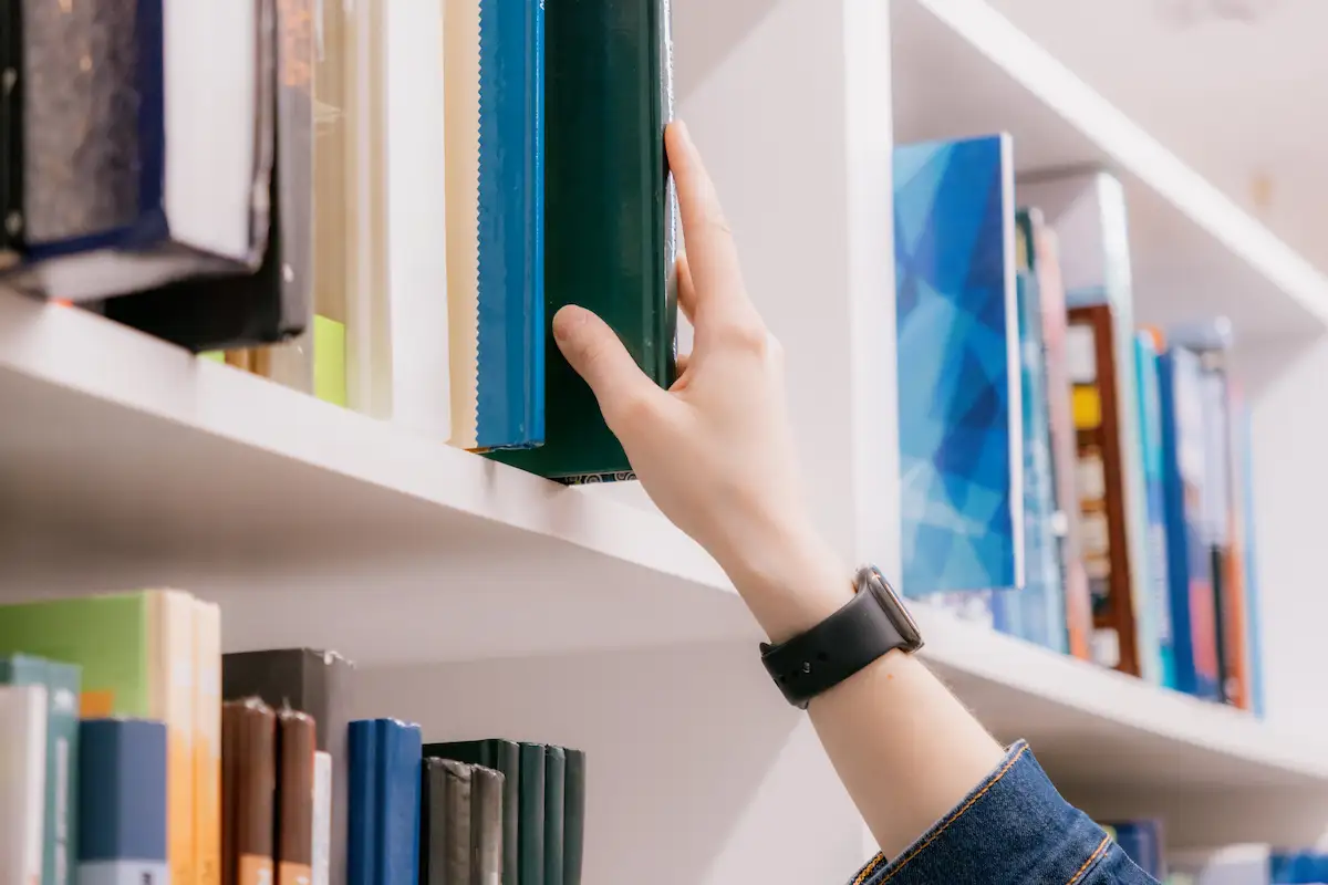 Hand picking up a book from a bookshelf