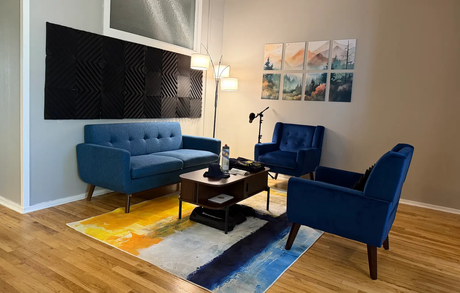 Podcast Studio with a blue couch, two blue chairs, a brown coffee table, a lamp, and sound absorption panels on the walls.