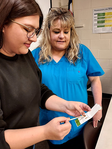 Jenny Duran is checking the stool for blood by performing a stool hemoccult test while her Medical Assisting instructor, Yvette O’Brien, looks on.